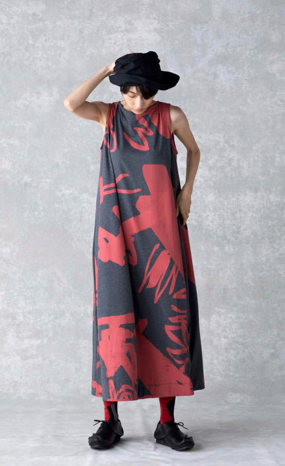 Front full body view of a woman wearing the moyuru art print dress. This sleeveless dress is charcoal with a red abstract print and a-line silhouette.