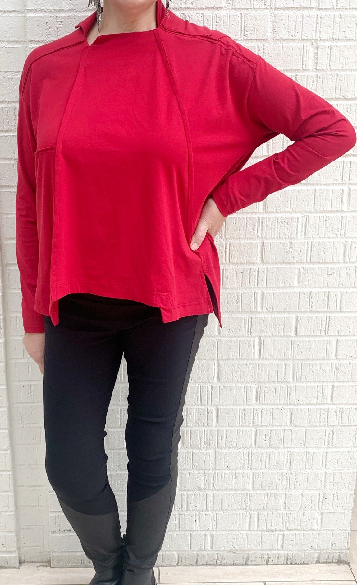 Front full body view of a woman wearing black pants and the moyuru red pullover top. This top has long sleeves, a boxy fit, and an asymmetrical hem.