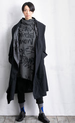 Load image into Gallery viewer, Front full body view of a woman wearing black pants, a black jacket, and the moyuru charcoal scribble tunic. This tunic is dark grey with a graffiti/scribble print all over it. The Tunic has long sleeves and a cowl neck.
