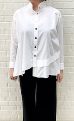 Load image into Gallery viewer, Front top half view of a woman wearing the moyuru white shirt. This shirt has a button down front, a stand collar, long sleeves, and an asymmetrical hem.

