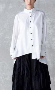 Front top half view of a woman wearing the moyuru white shirt. This shirt has a button down front, a stand collar, long sleeves, and an asymmetrical hem.