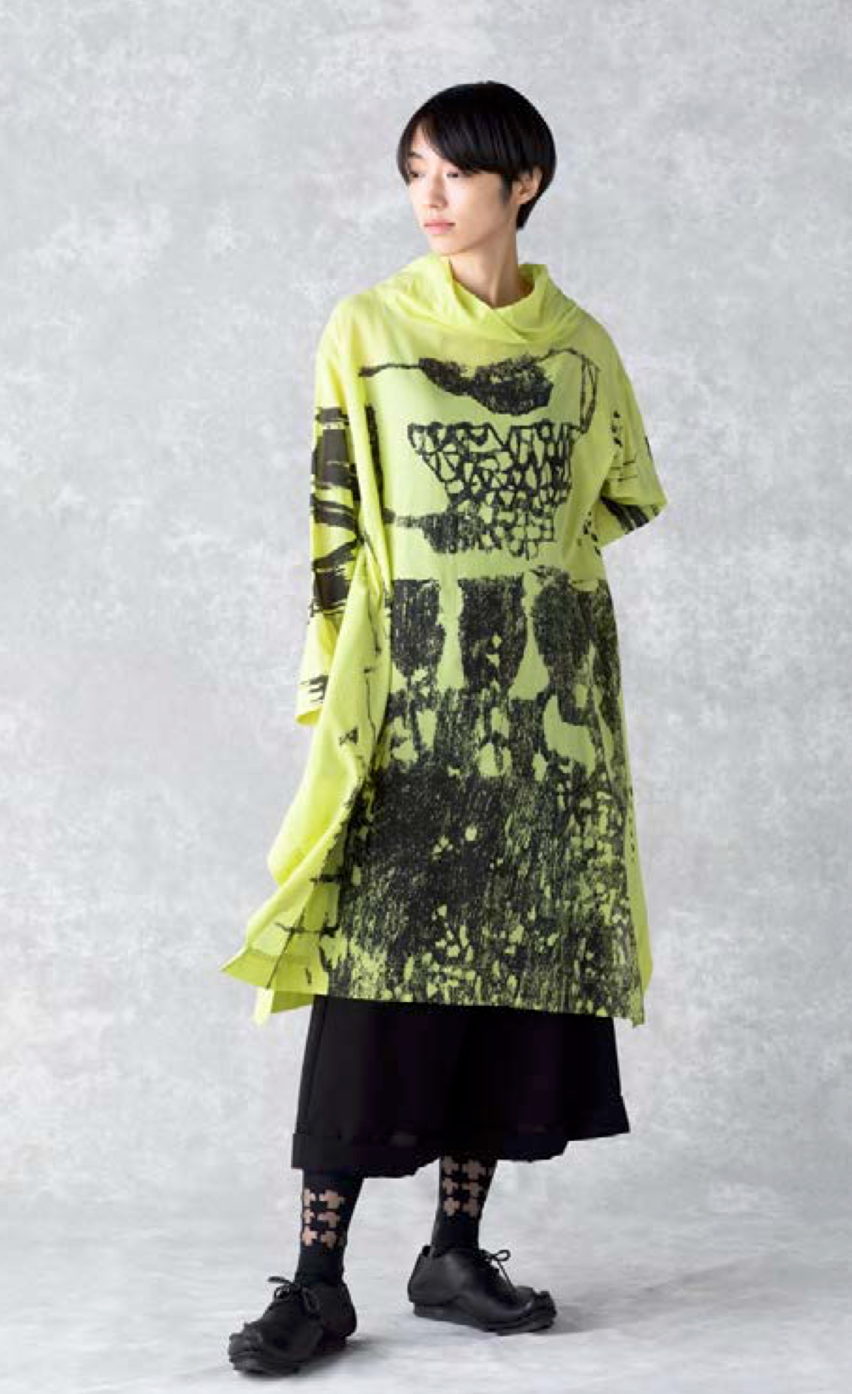 Front full body view of a woman wearing the moyuru art print tunic. This tunic is yellow with black abstract print, a cowl neck, long sleeves, and a hem that sits below the knees.