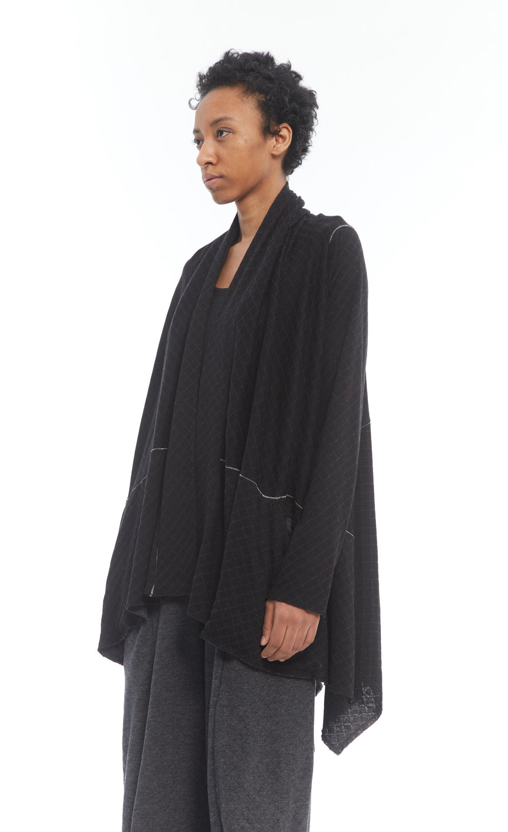 Front top half view of a woman wearing the mxmatthildur beth cardigan. This cardigan has long sleeves and a draped open front. The cardigan is black with ivory stitching.