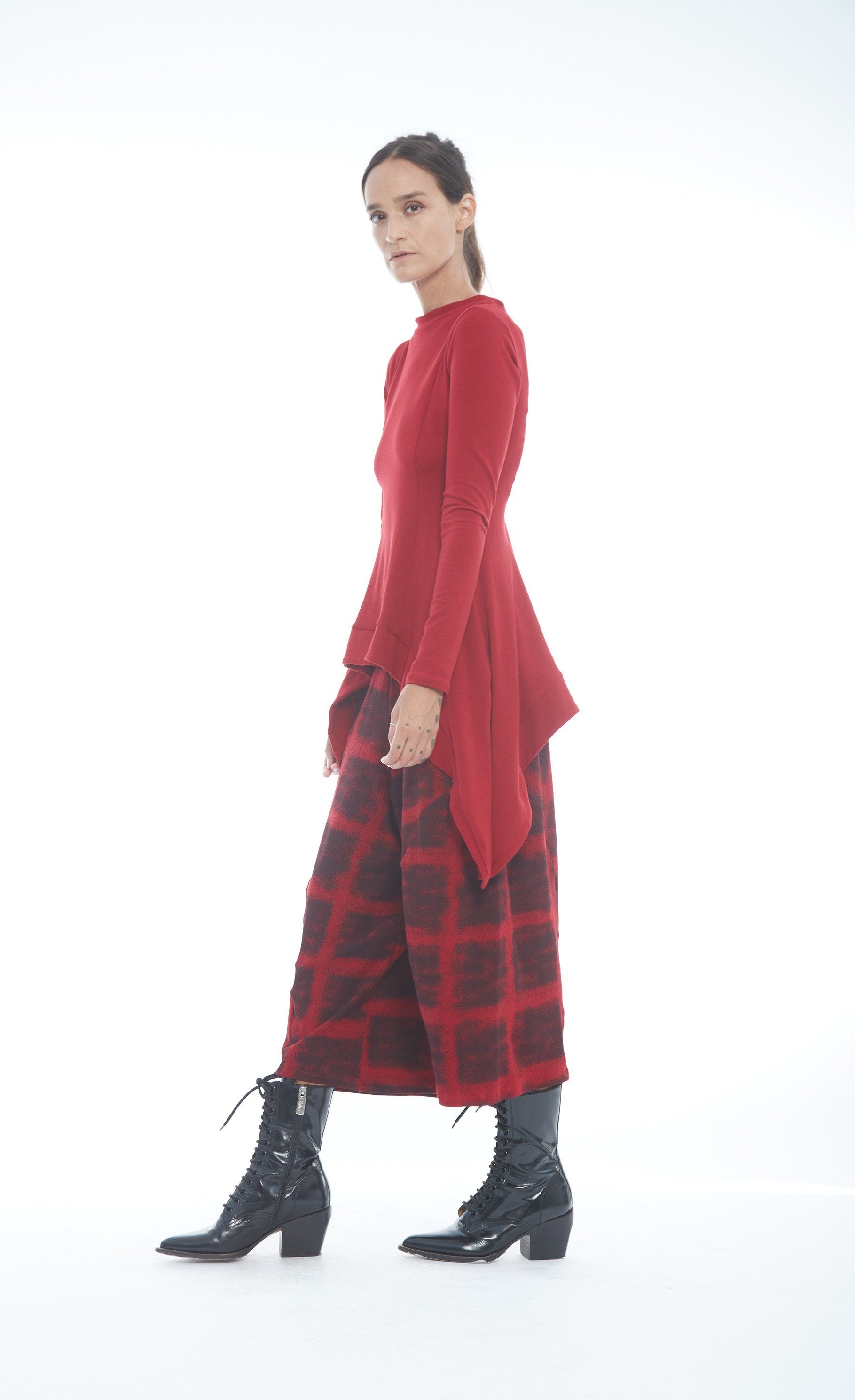 Front left side full body view of a woman wearing the mxmatthidlur lana top in red. This top has long sleeves, longer sides, and a high boat neck.