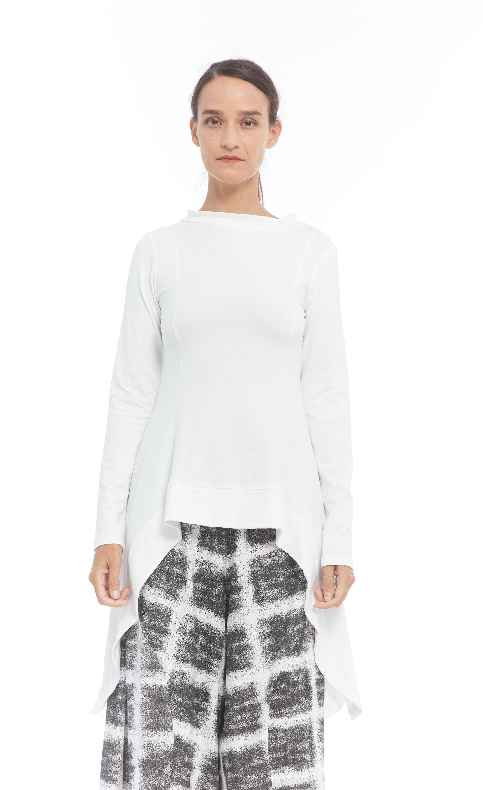 Front top half view of a woman wearing the mxmatthidlur lana top in white. This top has long sleeves, longer sides, and a high boat neck.