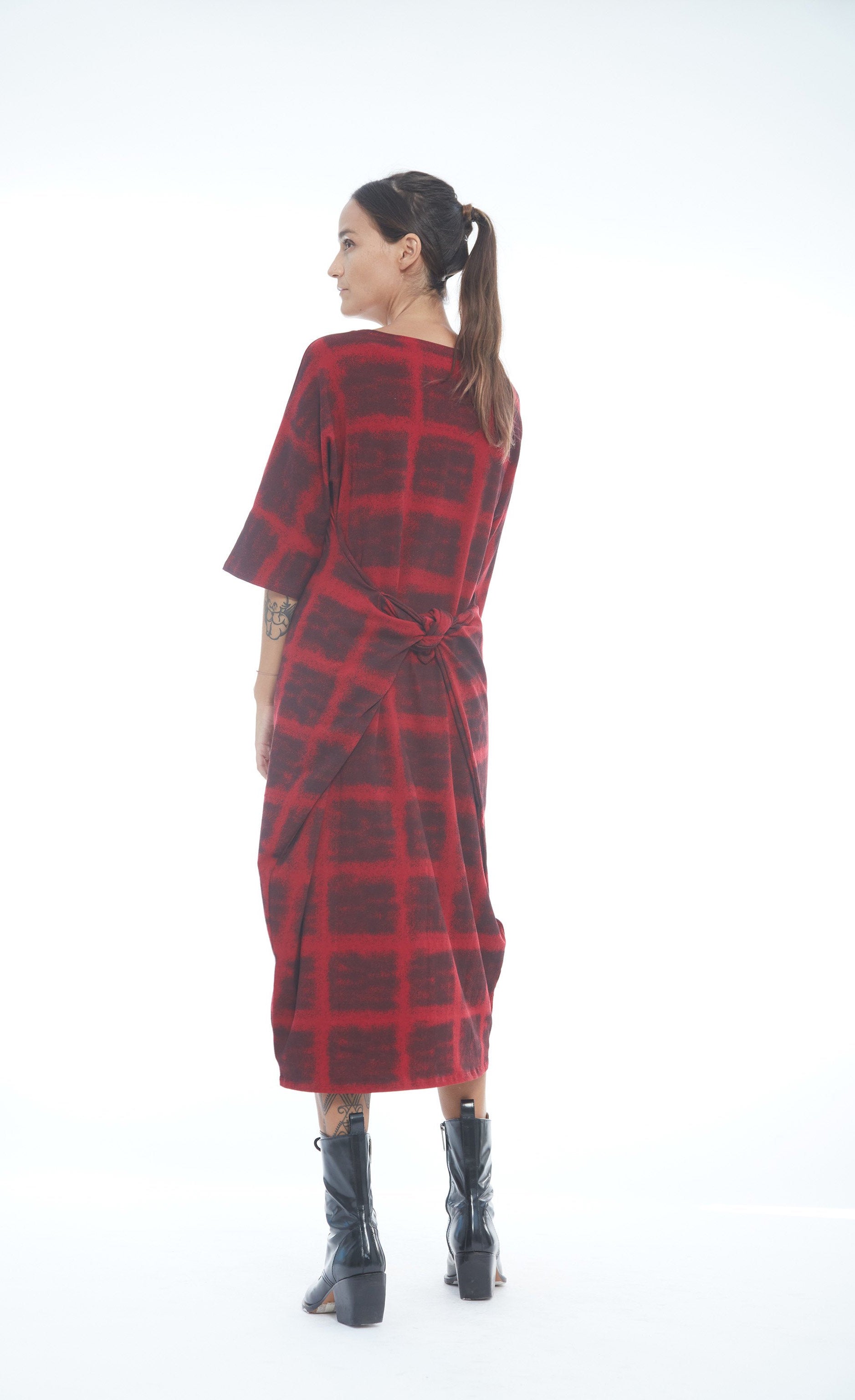Back full body view of a woman wearing the mxmatthildur mavis dress in a red and black plaid print. This dress has 3/4 length sleeves, and large pockets that are pulled to the back and tied together.