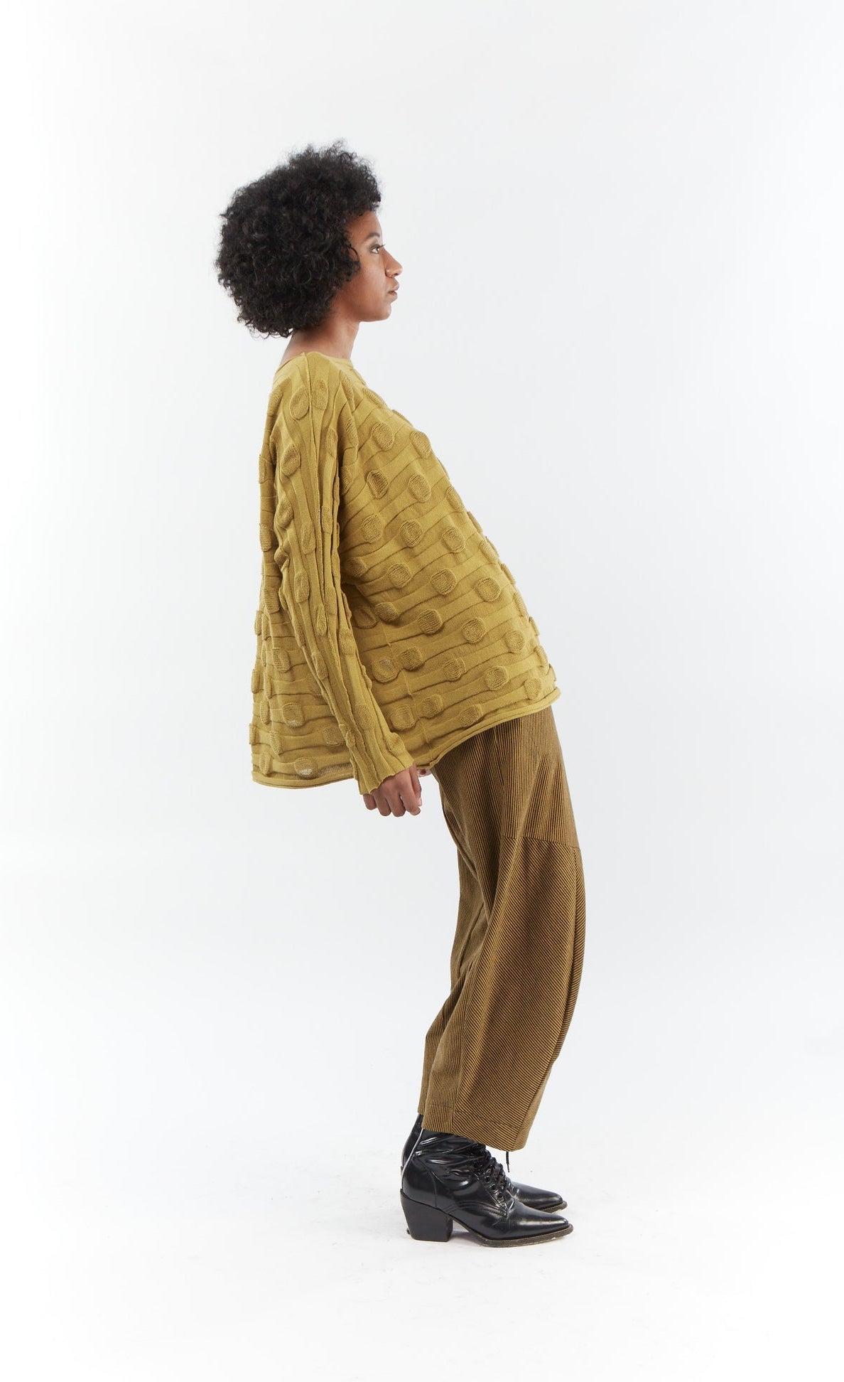 Right side full body view of a woman wearing the mxmatthildur bubble sweater and the matching mustard and black striped pants. This sweater features a bubble/jacquard textured fabric print, long sleeves, a boxy shape, and a boat neck.
