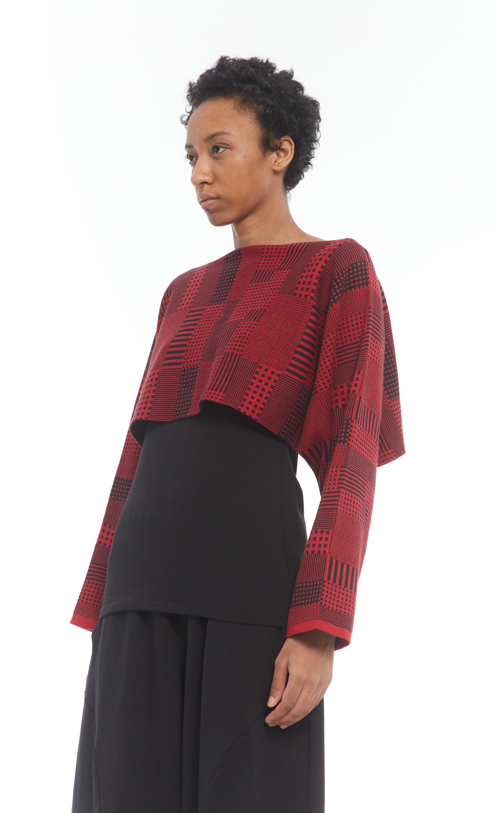 Front top half view of a woman wearing the mxmatthildur vonji sweater. This sweater is red and black plaid patchwork. The sweater has long sleeves and is being work as a cropped top.