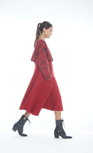 Front right side full body view of a woman wearing the mxmatthildur vonji sweater. This sweater is red and black plaid patchwork. The sweater has long sleeves and is being worn as a cropped topper with a red dress.
