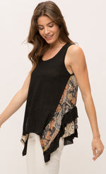 Load image into Gallery viewer, left sided, top half view of a woman wearing the Mystree Sleeveless Ruffle Hem Top. This tank top has a solid black front with mixed floral print running slightly slanted and vertically down the sides. The sides are longer than the rest of the shirt and the back has floral print and solid black ruffles.
