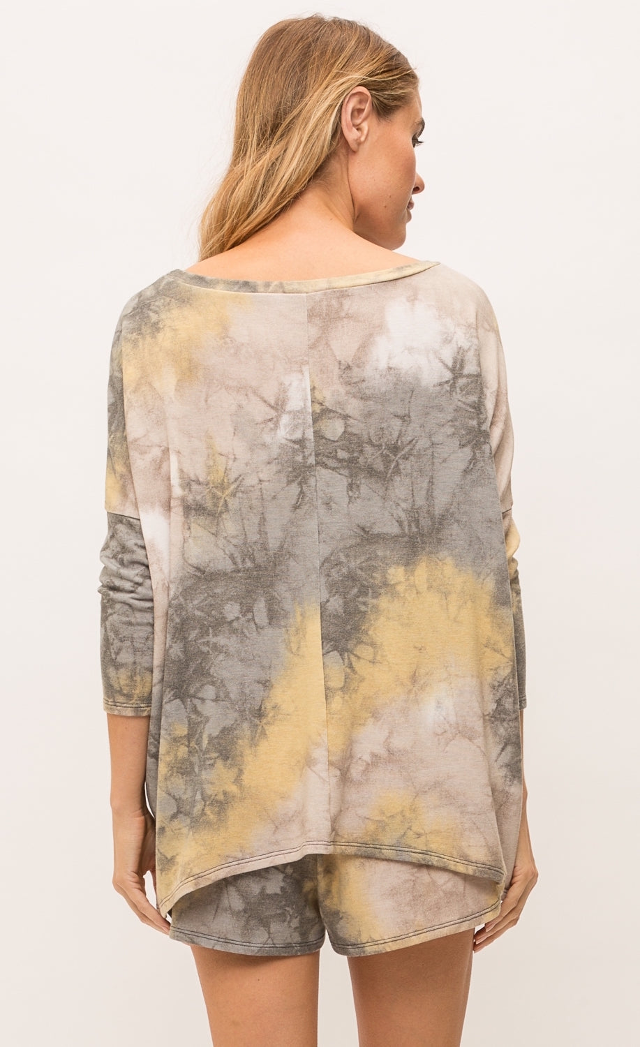 Back top half view of a woman wearing the mystree bluestone tie dye top. This top is a grey and yellow tie top with long sleeves and a boxy fit.