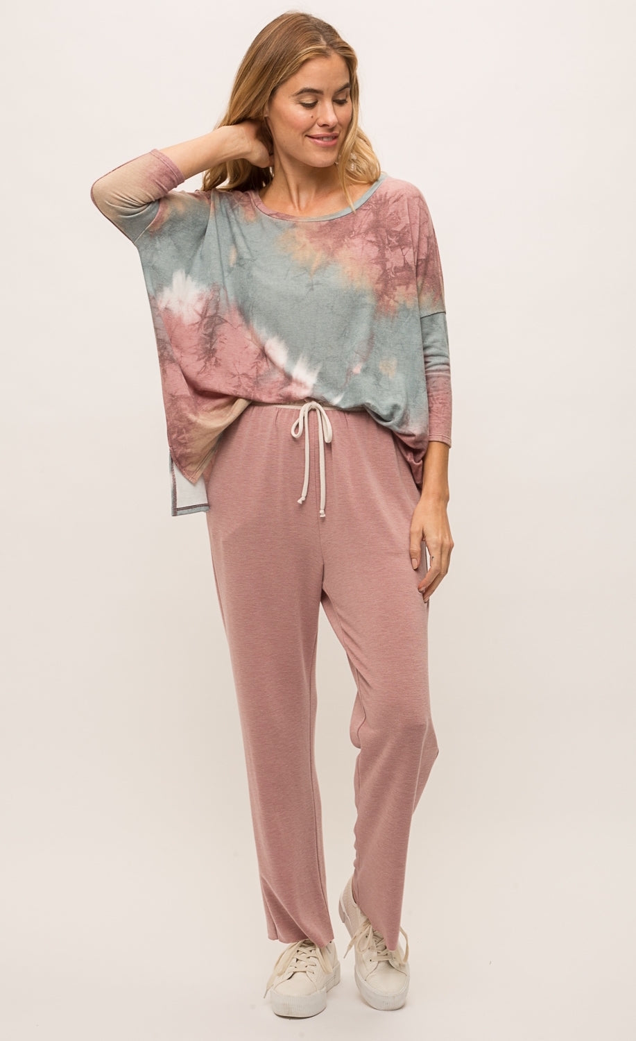 Front full body view of a woman wearing the mystree vintage tie dye top and the mystree lounge pant. The top is pink and blue tie dye and has long drop shoulder sleeves and a boxy fit. The bottoms are burgundy pink with a relaxed fit, pockets, and a white waistband.