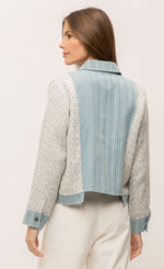 Load image into Gallery viewer, Back top half view of a woman wearing the Mystree Mix Media Jean Jacket with an off-white pant. This jacket has a striped denim body with woven grey and blue sleeves and sides. The sleeves have a denim hem and the sides of the jacket have a stepped unfinished denim hem. 
