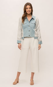 Front full body view of a woman wearing the Mystree Mixed Media Jean Jacket closed with an off-white pant. This jacket has a striped denim body with woven grey and blue sleeves and sides. The front has two patch breast pockets and a button up front. 