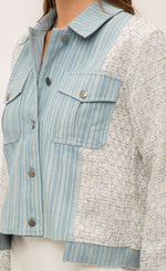 Load image into Gallery viewer, Front left sided close up view of the button up front and left breast pocket on the Mystree Mixed Media Jean Jacket. This jacket is being worn closed and has a striped denim body with woven grey and blue sleeves and sides. 
