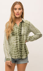 Load image into Gallery viewer, Front top half view of a woman with her left hand on her hip. She is wearing jean shorts and the Mystree Flowy Tie Dye Shirt. The shirt is olive green tie dyed with a hidden button up front, two breast pockets and long sleeves.
