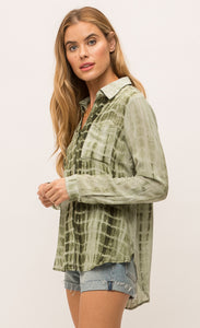 Left sided, top half view of a woman wearing the Mystree Flowy Tie Dye Shirt. The shirt is olive green tie dyed with a hidden button up front, two breast pockets and long sleeves.