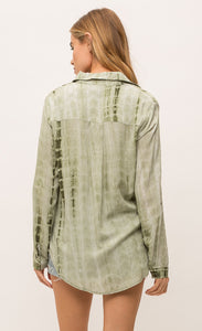 Back top half view of a woman jean shorts and the Mystree Flowy Tie Dye Shirt. The shirt is olive green tie dyed with a rounded hem and long sleeves.