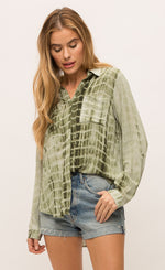 Load image into Gallery viewer, Front top half view of a woman with her thumb in the pocket of her jean shorts. On the top she is wearing the Mystree Flowy Tie Dye Shirt. The shirt is olive green tie dyed with a hidden button up front, two breast pockets and long sleeves.
