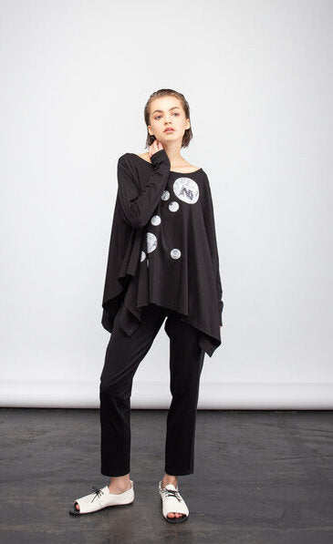 front full body view of a woman wearing the ny77 design circle top. This top is black and flowy with fitted long sleeves. On the front of the top are different sized circles with black and white comic book print.