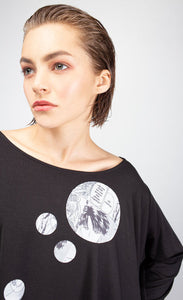 front close up view of the dots on the ny77 design circle top a woman is wearing. This top is black and flowy. On the front of the top are different sized circles with black and white comic book print.
