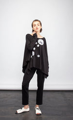 Load image into Gallery viewer, front full body view of a woman wearing the ny77 design circle top. This top is black and flowy with fitted long sleeves. On the front of the top are different sized circles with black and white comic book print.
