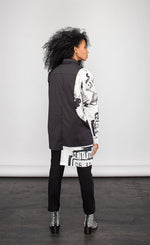 Load image into Gallery viewer, Front full body view of a woman wearing the ny 77 design mixed shirt. This shirt is predominately black. It has long sleeves. The left side of the shirt is solid black. The right side of the shirt is white with abstract sketched print on it. The right side&#39;s hem is longer than the left.
