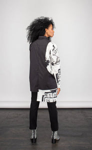 Front full body view of a woman wearing the ny 77 design mixed shirt. This shirt is predominately black. It has long sleeves. The left side of the shirt is solid black. The right side of the shirt is white with abstract sketched print on it. The right side's hem is longer than the left.