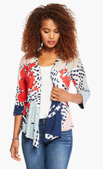 Load image into Gallery viewer, Front top half view of a woman wearing the nic+zoe art scene 4-way cardigan. This cardigan has a multicolored red, blue, and tan print on a white base. The cardigan also has an open front and a pointed hem. 
