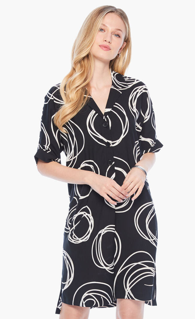 Front full body view of a woman wearing the nic+zoe billow dress. This dress is black with white swirl print all over it. The dress has a 3/4 button up front, elbow length sleeves, and front pockets.