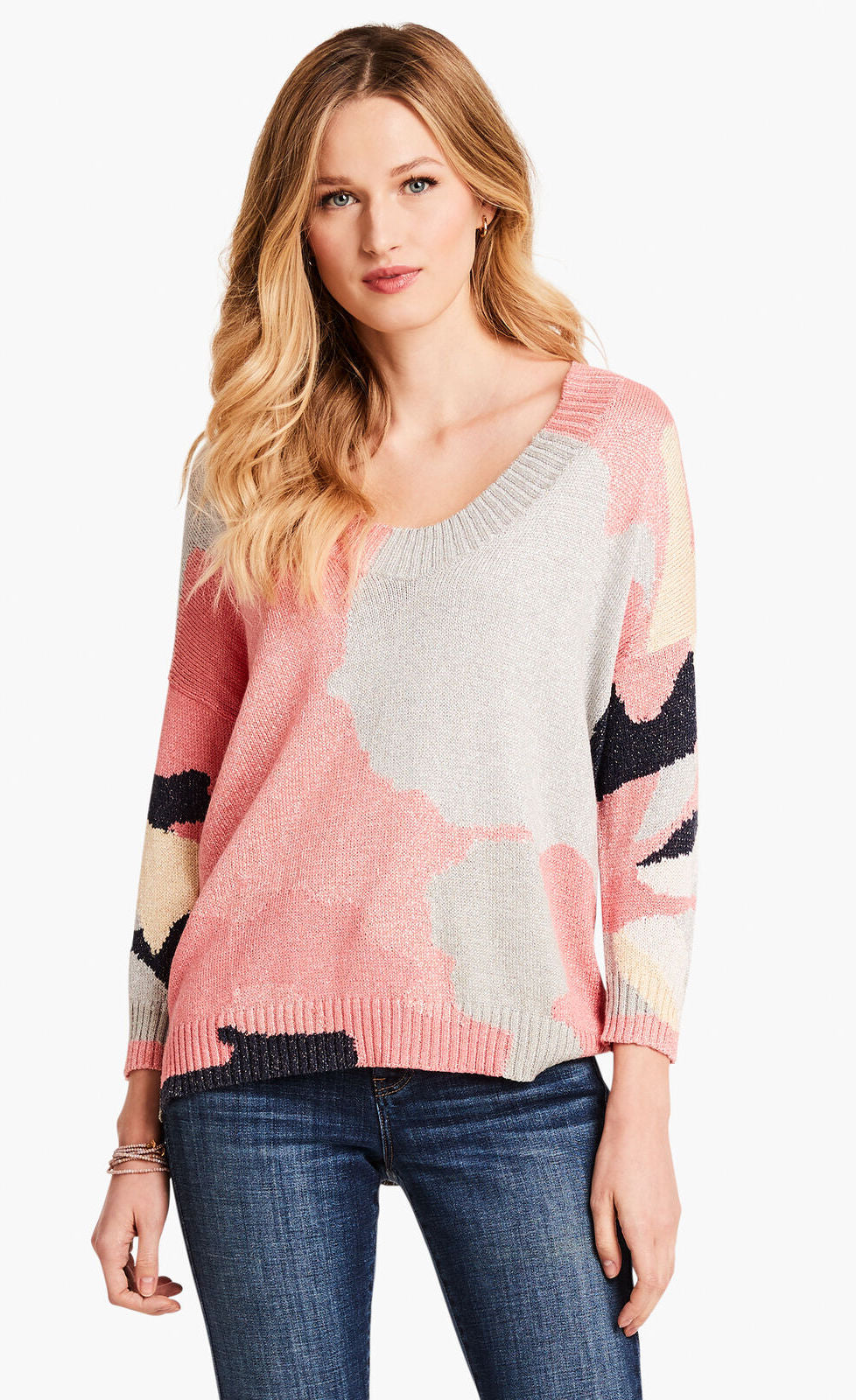 Front top half view of a model wearing the nic+zoe citrus splash sweater. This sweater is mainly pink with abstract colors of grey, blue, and creme all over it. This sweater has long sleeves, and a v-neck.