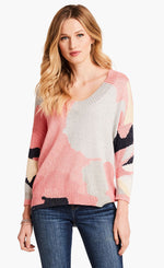 Load image into Gallery viewer, Front top half view of a model wearing the nic+zoe citrus splash sweater. This sweater is mainly pink with abstract colors of grey, blue, and creme all over it. This sweater has long sleeves, and a v-neck.
