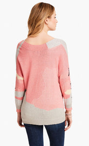 Back top half view of a model wearing the nic+zoe citrus splash sweater. This sweater is mainly pink with abstract colors of grey, blue, and creme all over it. This sweater has long drop shoulder sleeves.