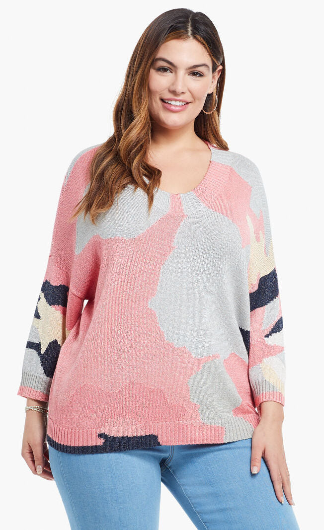 Front top half view of a model wearing the nic+zoe citrus splash sweater in a plus size. This sweater is mainly pink with abstract colors of grey, blue, and creme all over it. This sweater has long sleeves, and a v-neck.