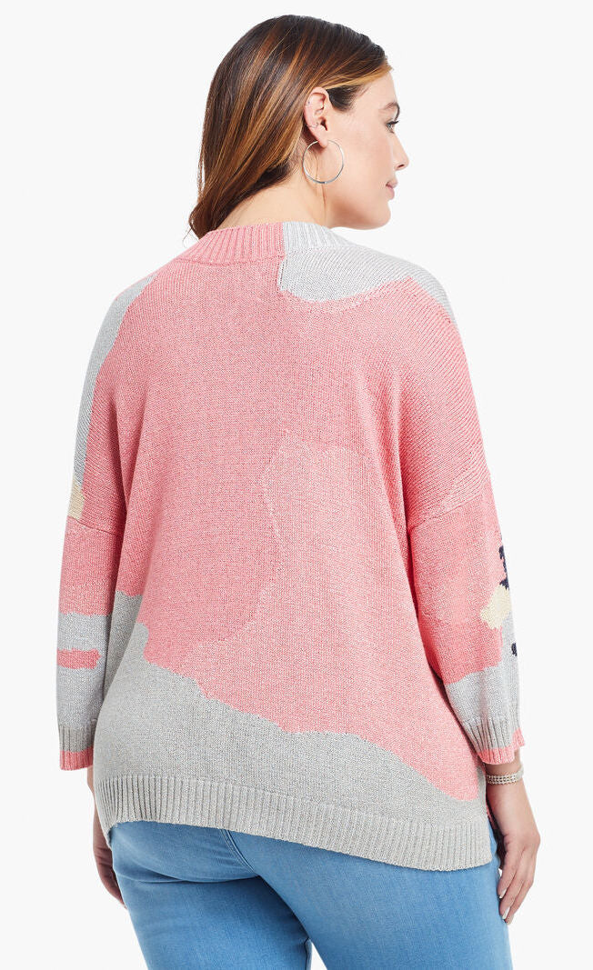 Back top half view of a model wearing the nic+zoe citrus splash sweater in a plus size. This sweater is mainly pink with abstract colors of grey, blue, and creme all over it. This sweater has long drop shoulder sleeves.