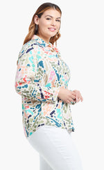 Load image into Gallery viewer, Right side, top half view of a woman wearing the nic+zoe color splash shirt. This shirt has a button up front, shirt collar, and long sleeves pushed up. It is multicolored with blue, pink, green, and salmon dots and strokes.
