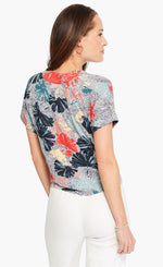Load image into Gallery viewer, back top half view of a woman wearing white pants and the nic+zoe fan dot tie top. This top has short sleeves and a white background with navy dots and fanned navy, red, and nude flowers all over it.
