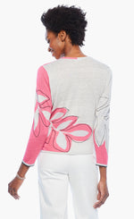 Load image into Gallery viewer, Back top half view of a woman wearing the nic+zoe hibiscus tie sweater. This sweater has a wrap look with a faux side tie. The back is white with a pink hibiscus flower while the sleeves are pink and white. The sweater has 3/4 length sleeves.
