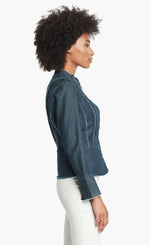 Load image into Gallery viewer, Side, top half view of a woman wearing white pants and the Nic + Zoe Favorite Denim Jacket. The dark denim jacket features frayed stitching, a cropped cut, and a short stand collar.
