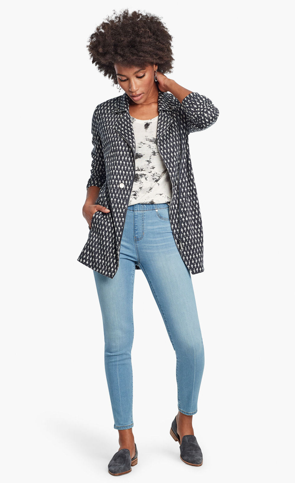 Front, full body view of a woman wearing the Nic + Zoe Ponte Ikat Jacket over a white printed top and with fitted jeans. The jacket is indigo with a white speck print all over it. It has a flat, notched lapel, and a front, off-center zipper.