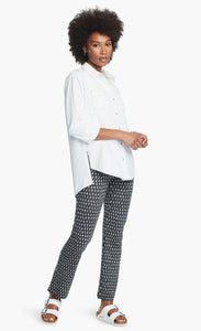 Front full body view of a woman wearing a white button down shirt and the Nic + Zoe Ponte Ikat Pant. These pants are indigo with white speckled print. They have a straight leg and sit above the ankles.