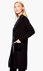 Load image into Gallery viewer, Left side top half view of a woman wearing the nic+zoe royal trimmings jacket and black leggings. This jacket is black with faux leather trim and two faux leather front pockets. The jacket has long sleeves and goes down to the knees.
