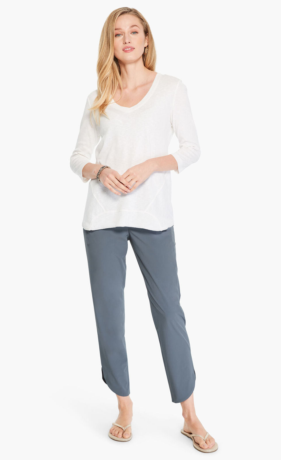 Front full body view of a woman wearing a white shirt and the Shirt Tail Tech Stretch Pant in slate grey. This pant has a straight leg, a cropped length, and an asymmetrical hem.