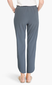 back bottom half view of a woman wearing the Shirt Tail Tech Stretch Pant in slate grey. This pant has a straight leg, a cropped length, and an asymmetrical hem.
