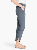 Load image into Gallery viewer, Right side, bottom half view of a woman wearing the Shirt Tail Tech Stretch Pant in slate grey. This pant has a straight leg, a cropped length, and an asymmetrical hem.
