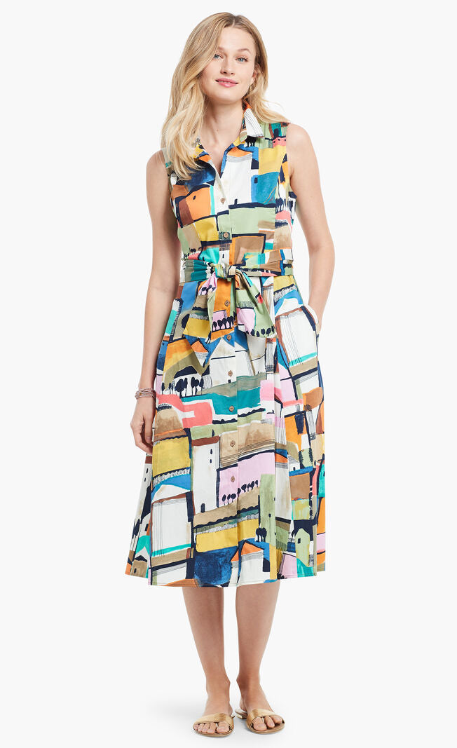 Front full body view of a woman wearing the nic + zoe street seen shirt dress. This dress has a colorful print of buildings. The front of the dress has a button down front, a collar, and a tie at the waist.