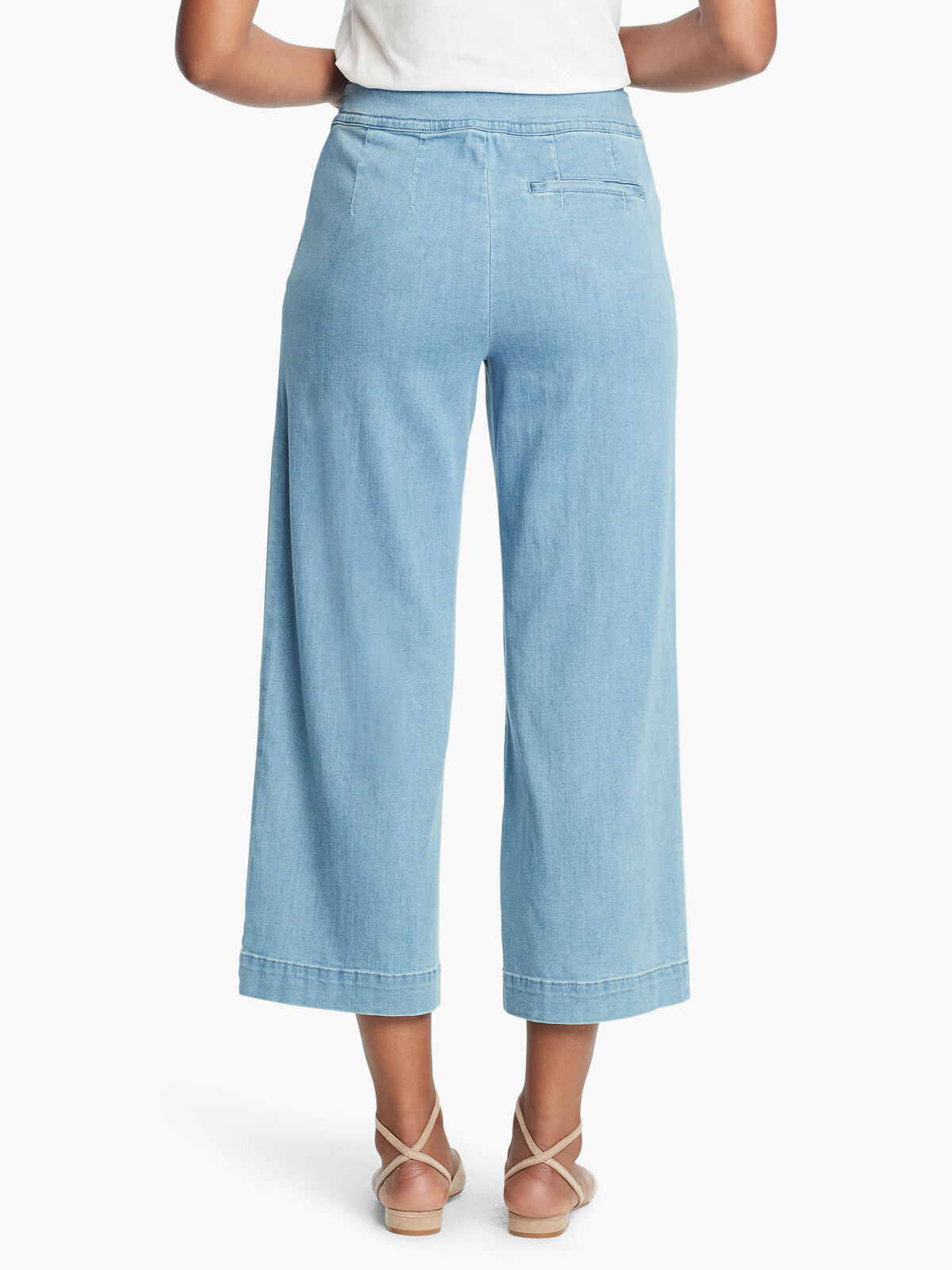 Back, bottom half view of a woman wearing a white top and the Nic + Zoe Summer day denim pant. These light wash jeans are wide legged and cropped. The back of these pants feature a pocket on the right side.