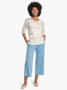 Front, full body view of a woman wearing a white sweater and the Nic + Zoe Summer day denim pant. These light wash jeans are wide legged and cropped with side pockets.