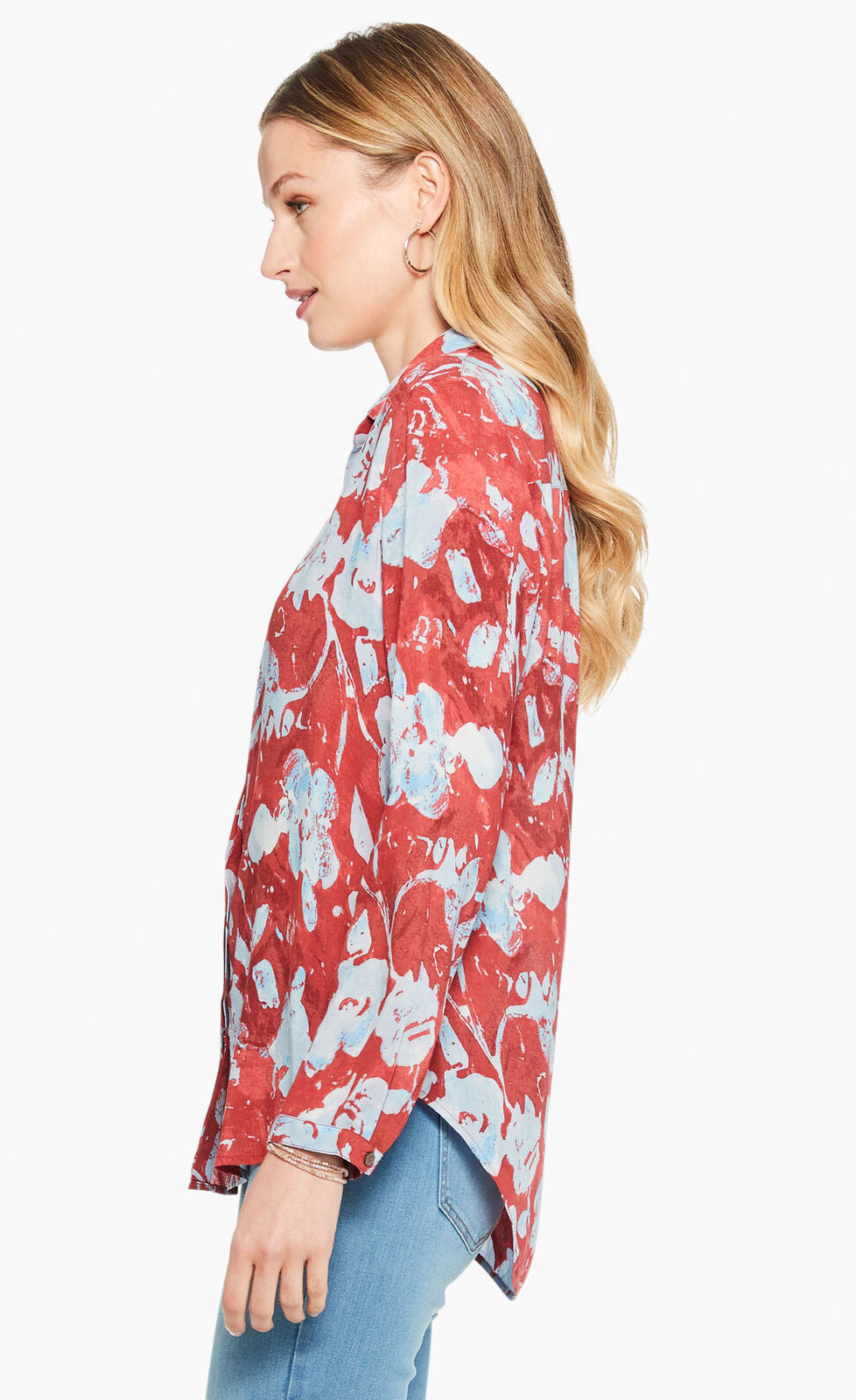 left side top half view of a woman wearing the terracotta blooms shirt from nic and zoe. This shirt has a relaxed fit with long sleeves and a button down front. The shirt is red with a light blue floral print.