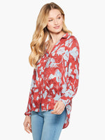 Load image into Gallery viewer, Front top half view of a woman wearing the terracotta blooms shirt from nic and zoe. This shirt has a relaxed fit with long sleeves and a button down front. The shirt is red with a light blue floral print.
